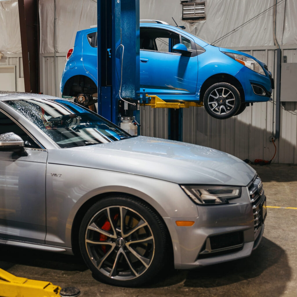 a grey car and blue car inside of a body shop in Houston, TX undergoing auto body work.